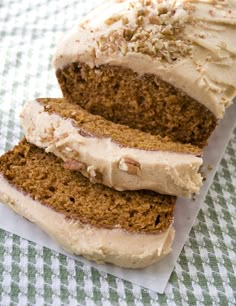 two slices of carrot bread with cream cheese frosting and nuts on top, sitting on a checkered table cloth