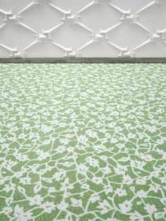 a green and white rug on the floor in front of a wall with an intricate pattern