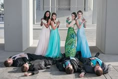 four women in long dresses posing on the ground with one man laying on the ground