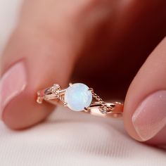 a woman's hand holding a ring with a white opal stone on it