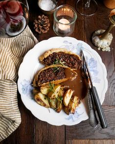 a white plate topped with meat and potatoes covered in gravy next to wine glasses