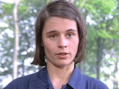 a woman in a blue shirt and tie looking at the camera with trees in the background