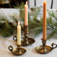 three candles sitting on top of a table next to pine branches