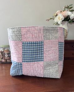 a pink and blue patchwork pillow sitting on top of a wooden table next to a vase with flowers