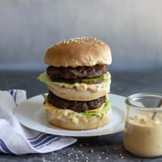 a hamburger sitting on top of a white plate next to a jar of mustard and ketchup