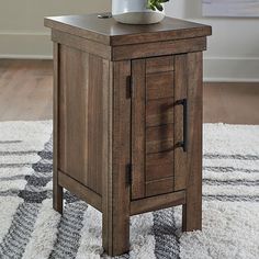 a small wooden table with a plant on top and a rug in the room next to it