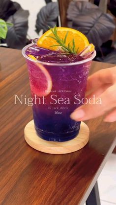 a purple drink with orange slices and rosemary garnish on the rim, sitting on a wooden table