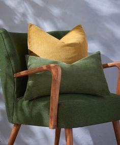 a green chair with two yellow pillows on it and a white wall behind the chair