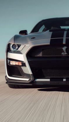 the front end of a black and silver sports car driving on a road with blurry background