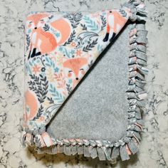 a gray and orange blanket with fringes on it sitting on a counter top next to a marble surface