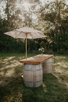 a wooden table with an umbrella over it in the middle of some grass and trees