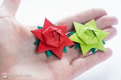 two origami flowers in the palm of someone's hand, one red and one green