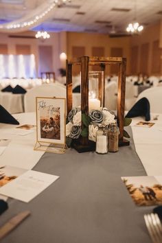 an arrangement of flowers and candles on a table in a banquet hall with white linens