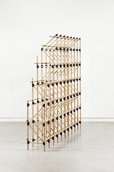 a sculpture made out of wooden sticks with black dots on the top and bottom, standing in an empty room