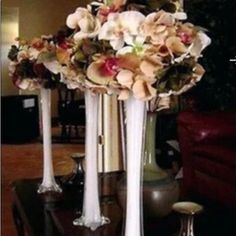 three tall white vases with flowers in them on a table next to a couch