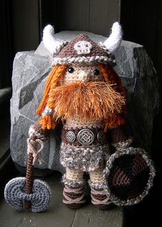 a crocheted viking doll is standing next to a rock