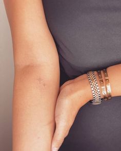 a woman's arm with two bracelets and a cross tattoo on the wrist