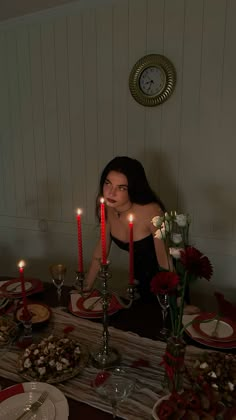 a woman sitting at a table with candles in front of her and plates on the table