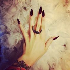 a woman's hand with black nail polish and ring on her left hand, surrounded by white feathers