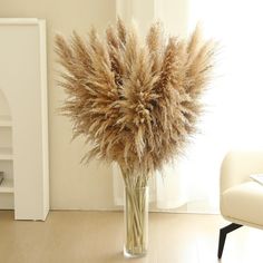 a vase filled with dry grass sitting on top of a hard wood floor next to a white chair