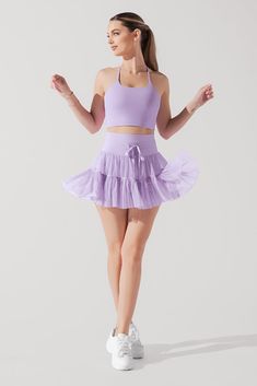 a woman wearing a purple skirt and tank top with her hands out in the air