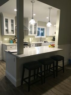 a kitchen with two stools in front of an island and three lights hanging from the ceiling