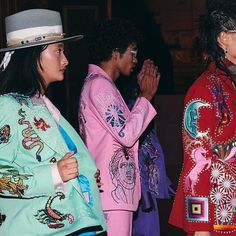 three people dressed in colorful clothing standing next to each other with hands together and one person wearing a hat