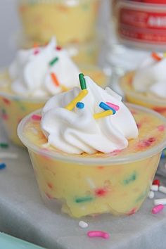 cupcakes with white frosting and sprinkles in plastic cups on a table