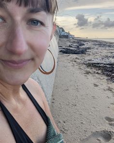 a woman standing on top of a sandy beach next to the ocean wearing large hoop earrings