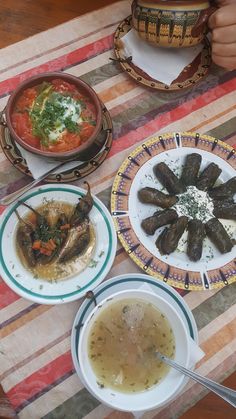 a table topped with plates of food next to bowls of soup and sauce on top of a striped table cloth