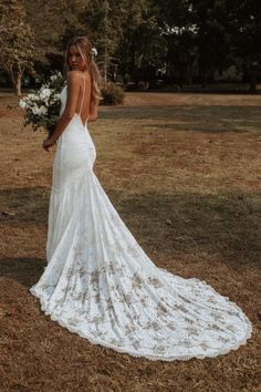 a woman in a white wedding dress standing on the grass with her back to the camera