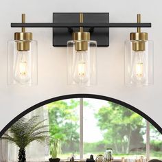 three light bathroom fixture with clear glass shades and brass accents in an arched window area