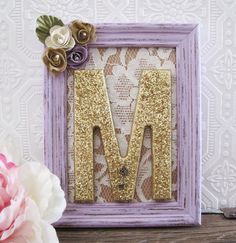 a wooden frame with the letter m on it and some flowers in front of it