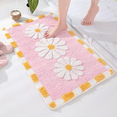 a person standing on a bed with a pink and yellow flowered rug next to it