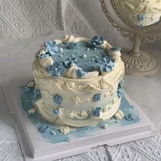 a white and blue cake sitting on top of a table next to a small mirror