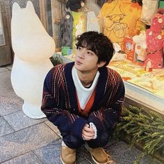 a young man sitting on the ground in front of a store window with stuffed animals behind him