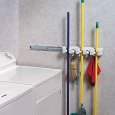 a washer and dryer in a bathroom next to a wall mounted rack with brooms