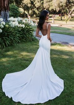 a woman in a white wedding dress standing on the grass with her back to the camera