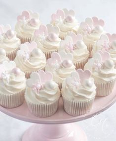 cupcakes with white frosting and pink decorations on a cake plate, ready to be eaten