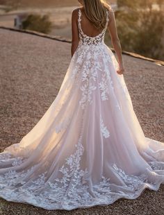 a woman in a wedding dress standing on top of a dirt road with her back to the camera