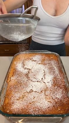 a woman is sprinkling sugar on top of a baked cake in a pan