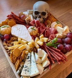 a wooden platter filled with cheeses, meats and other foods next to a human skull