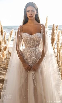 a woman in a wedding dress standing on the beach with her arms behind her back