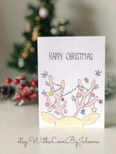 a handmade christmas card with reindeers on the front and side, in front of a christmas tree