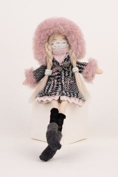 a doll is sitting on top of a box wearing a pink hat and coat with fur