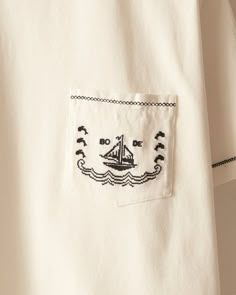 a white shirt with a sailboat embroidered on the front pocket and black stitching