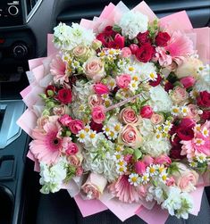 a bouquet of pink and white flowers sitting on top of a car dash board in front of a steering wheel