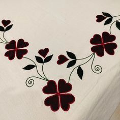 an embroidered tablecloth with red flowers and leaves on it, in the shape of hearts