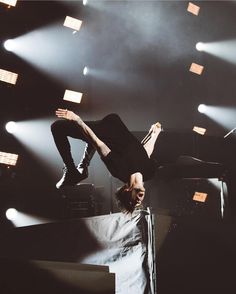 a man doing a handstand on top of a stage with lights in the background