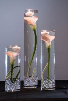 three clear vases with flowers in them on a black table top next to each other